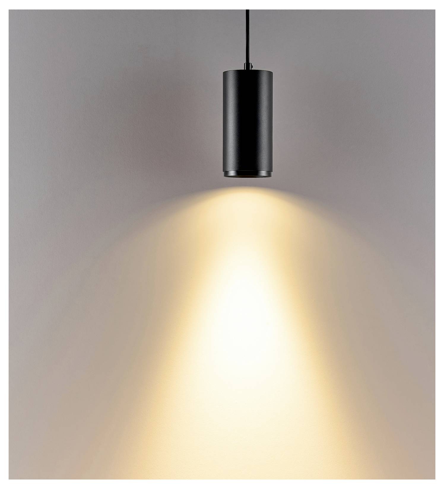 Suspension cylindrique noire projetant un cône de lumière chaleureuse sur un mur gris.