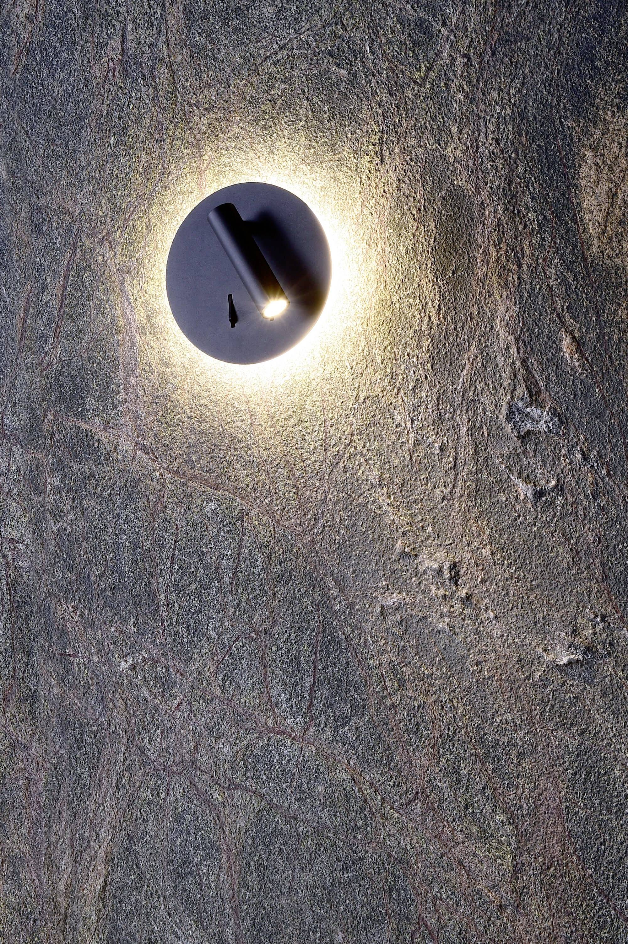 Lampe de forme circulaire qui projette une lumière chaleureuse sur un mur de pierre texturé.
