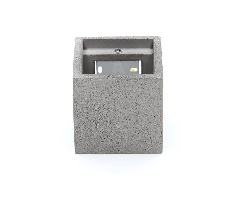 Un luminaire mural carré en béton gris. Contient une lampe LED à l'intérieur et est conçu pour être monté sur un mur.