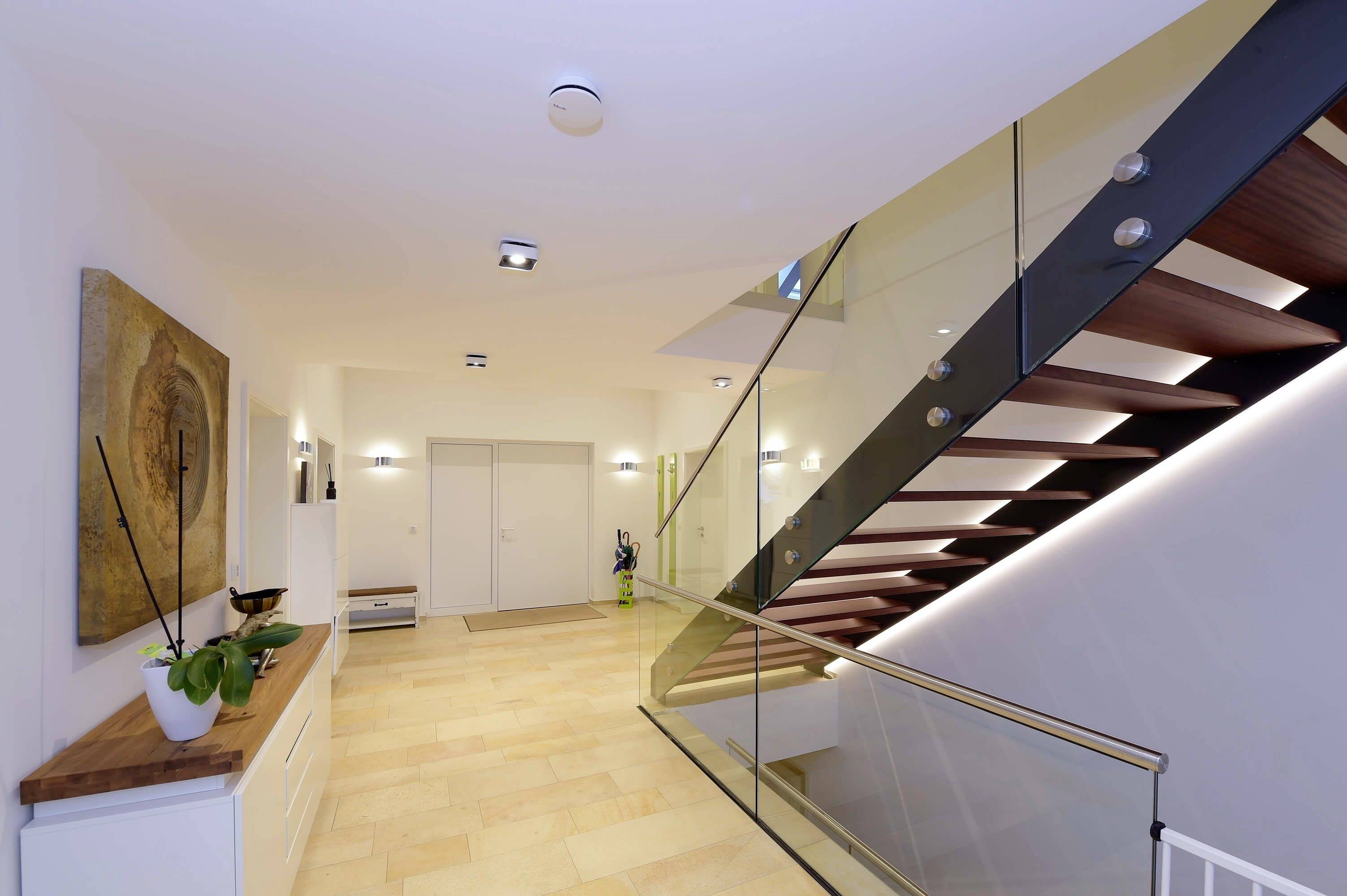 Entrée d'une maison moderne avec un escalier en bois et des éléments en verre, un placard avec des décorations à gauche et un escalier menant à l'étage à droite.