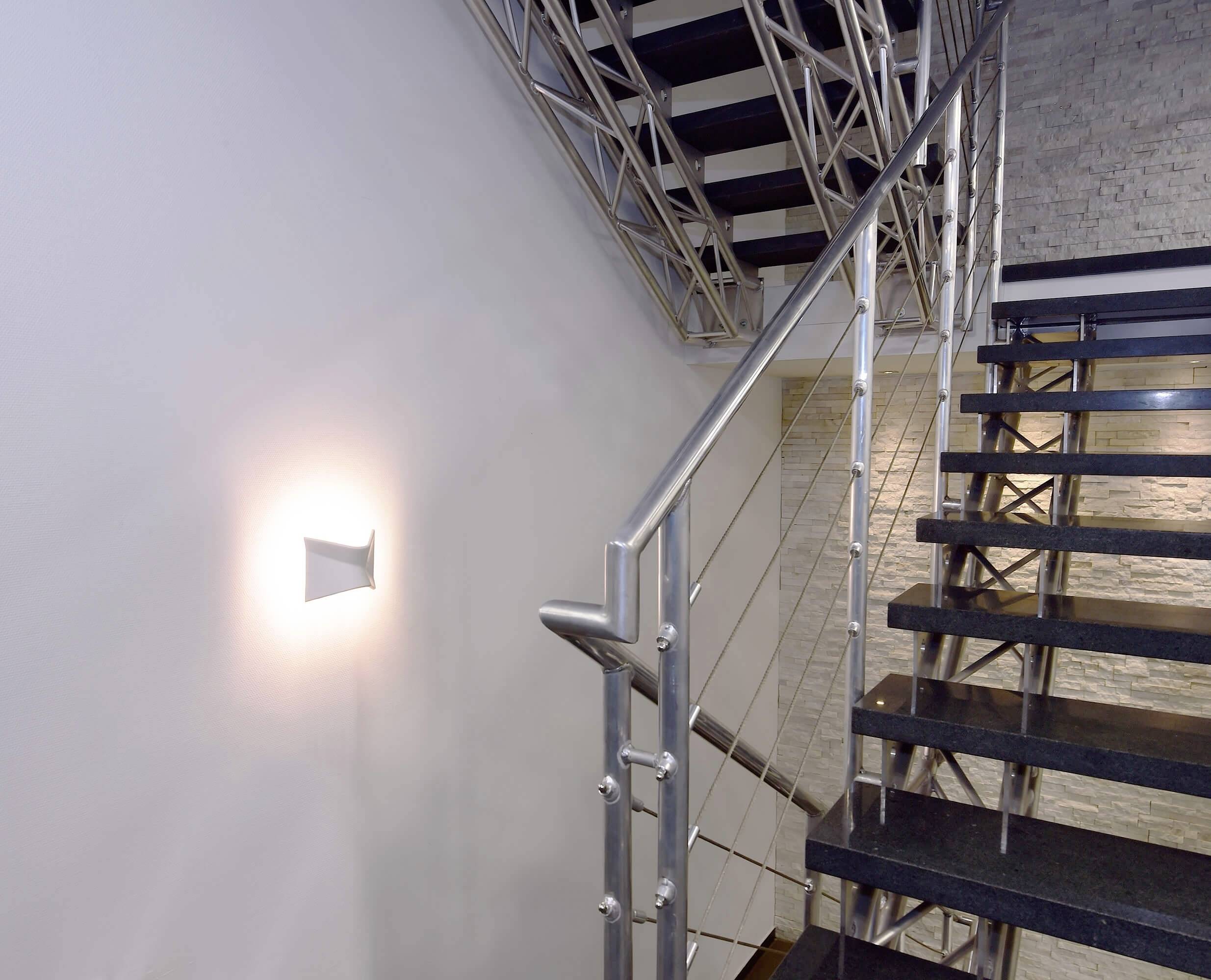Un escalier moderne en métal et bois avec un éclairage mural blanc minimaliste sur le côté. Cage d'escalier dans un bâtiment.