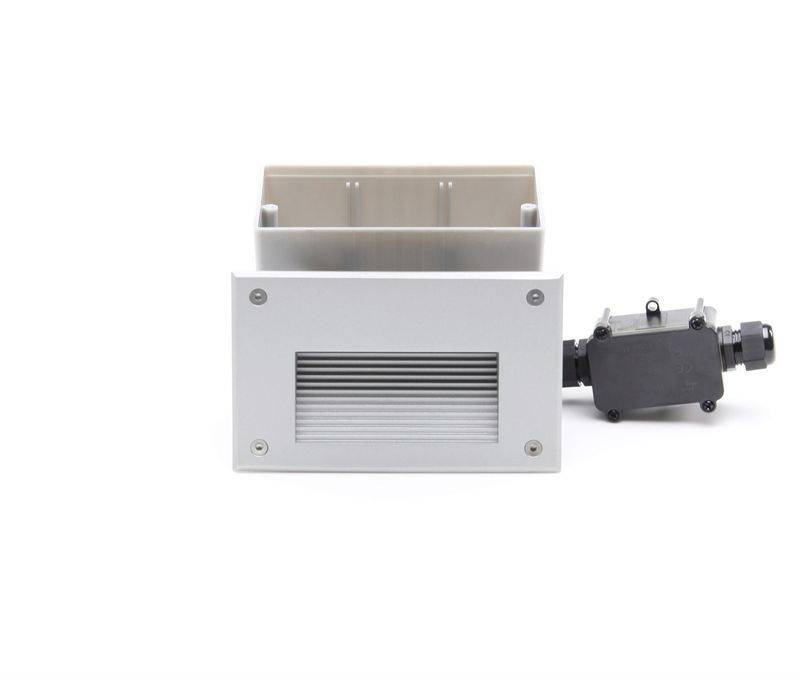 Un boîtier rectangulaire en métal avec une grille de ventilation, à côté duquel se trouve un petit boîtier de connexion noir avec un passe-câble.