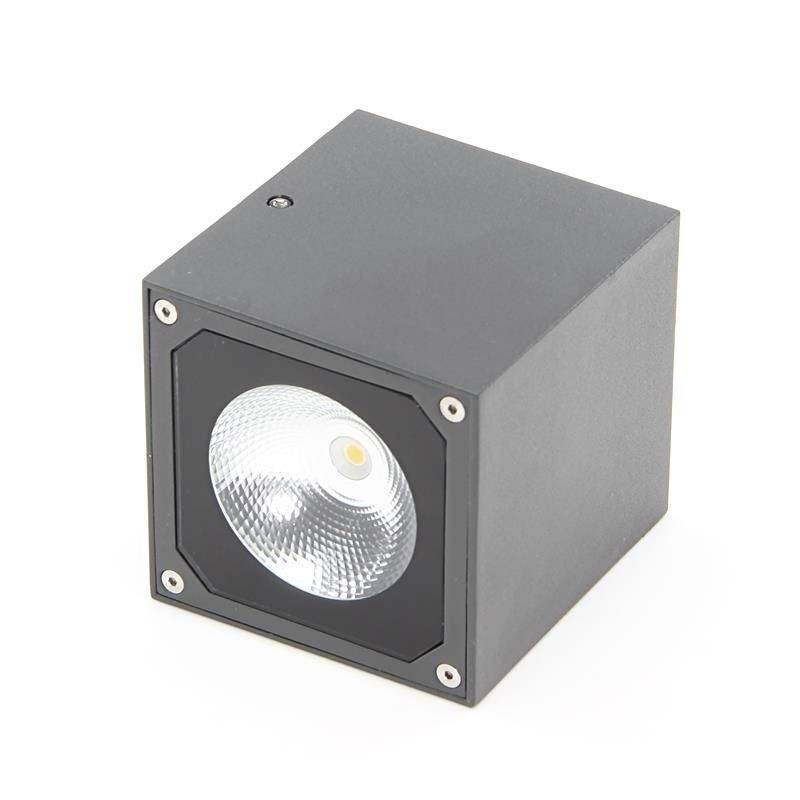 Un projecteur LED carré noir dans un boîtier métallique avec un unique faisceau lumineux circulaire au centre.