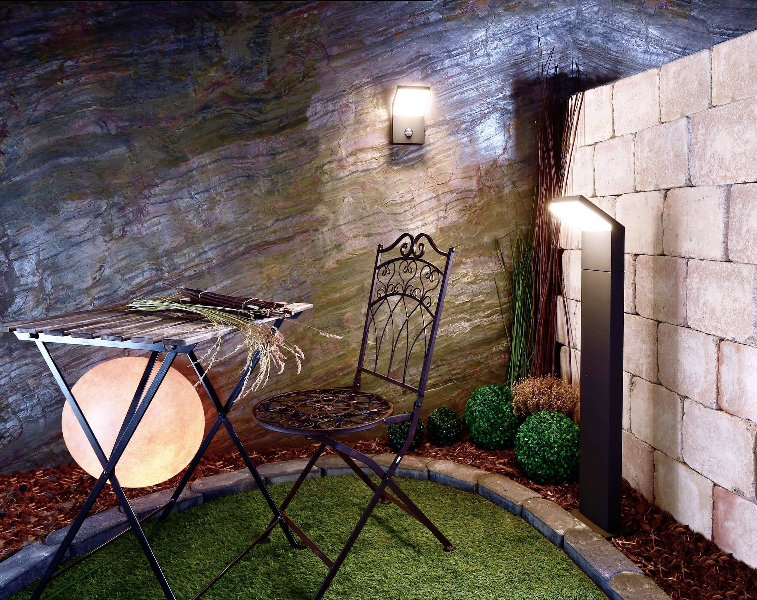 Un petit espace décoratif de jardin avec une table pliante, une chaise et un éclairage. De l'herbe artificielle et des plantes ornementales entourent l'endroit.