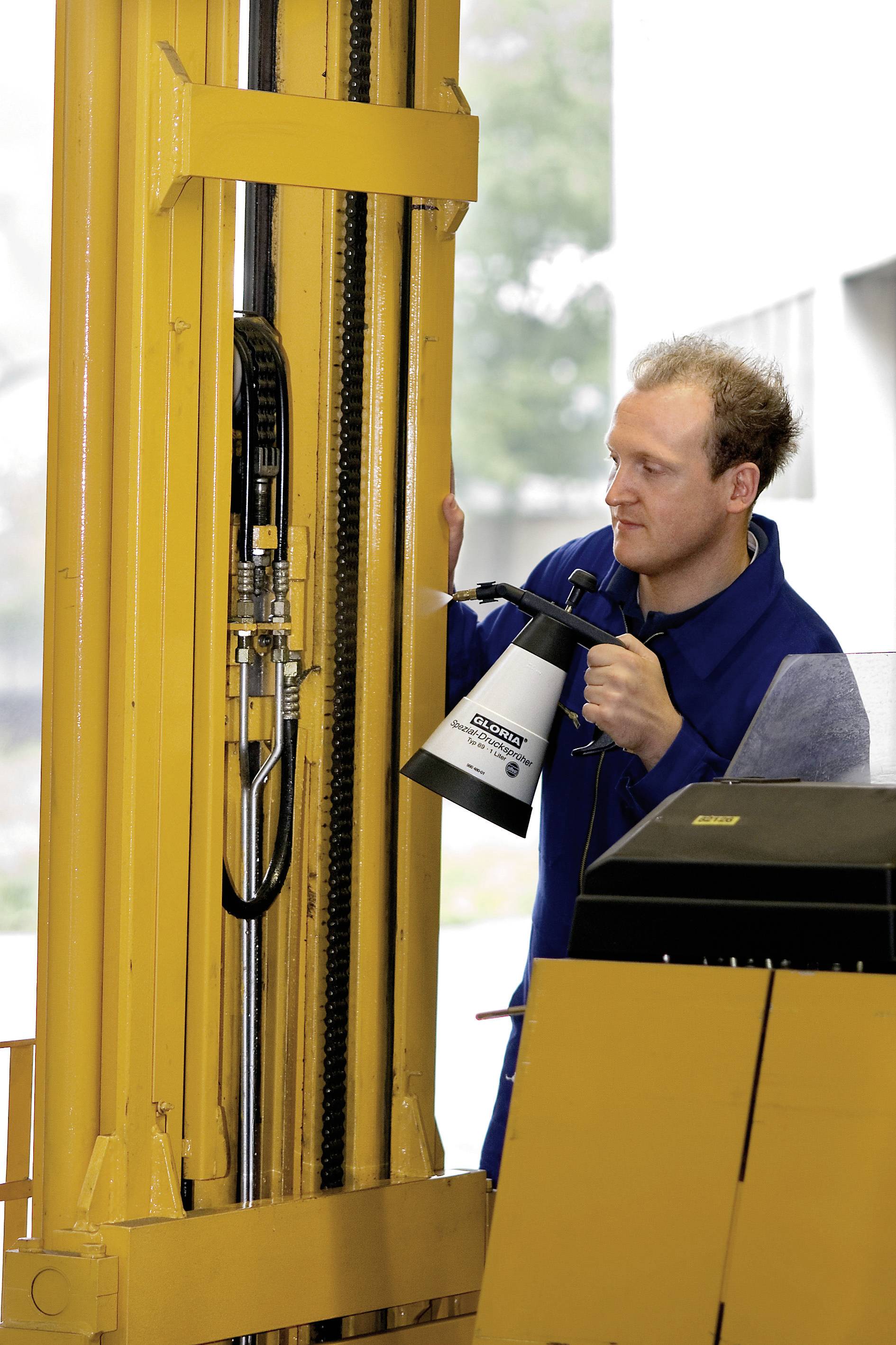 Un homme en tenue de travail inspecte le mécanisme d'un chariot élévateur jaune et tient une lampe pour une meilleure visibilité.