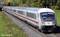 Un train Intercity rouge et blanc de la Deutsche Bahn circule sur une ligne ferroviaire à travers un paysage vert et boisé.