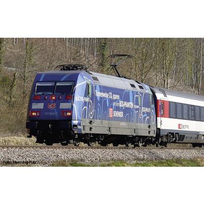 Un train de la Deutsche Bahn avec une locomotive bleue circule sur des rails à travers une région rurale, des arbres sont visibles sur la droite.