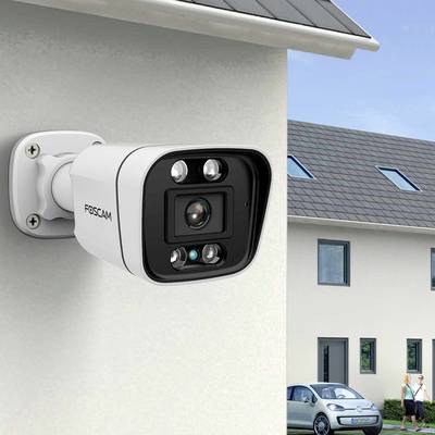 Caméra de surveillance montée sur le mur extérieur d'une maison, avec vue sur une voiture et un autre bâtiment en plein jour.