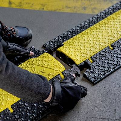 Une personne installe des plaques de couverture de câbles jaunes et noirs sur un sol. Les plaques portent un symbole d'avertissement.
