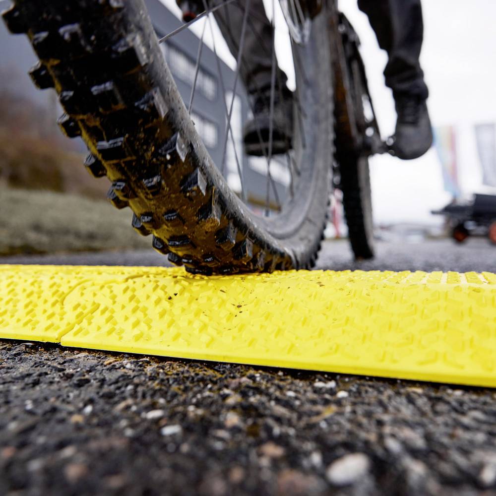 Un vélo roule sur un dispositif de voirie jaune et texturé sur une route. Ce dispositif est probablement destiné à améliorer la sécurité routière.
