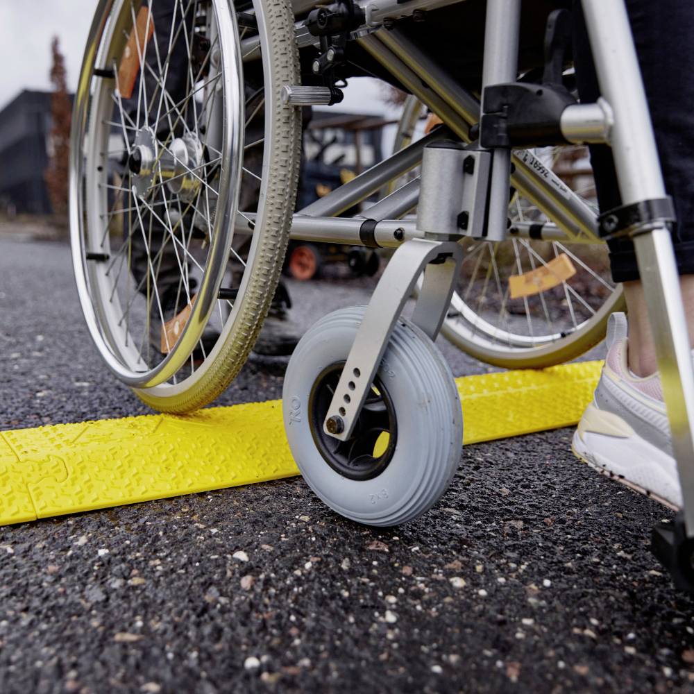 Un conducteur de fauteuil roulant traverse une rampe de rue jaune. La rampe facilite l'accès aux personnes à mobilité réduite.