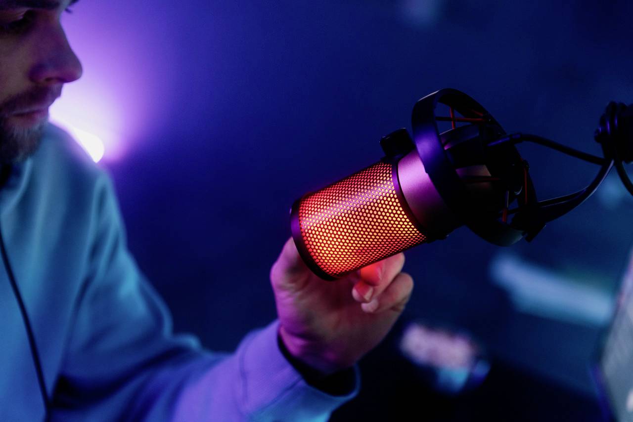Une personne tient un microphone rouge vif dans un studio. L'arrière-plan est éclairé d'un bleu sombre, créant une atmosphère médiatique.