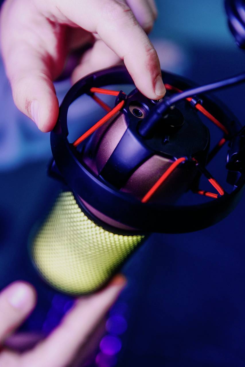 Une main ajuste un microphone de studio dans un amortisseur de vibrations. Le microphone a un boîtier vert et des éléments de suspension rouges en forme de toile d'araignée.