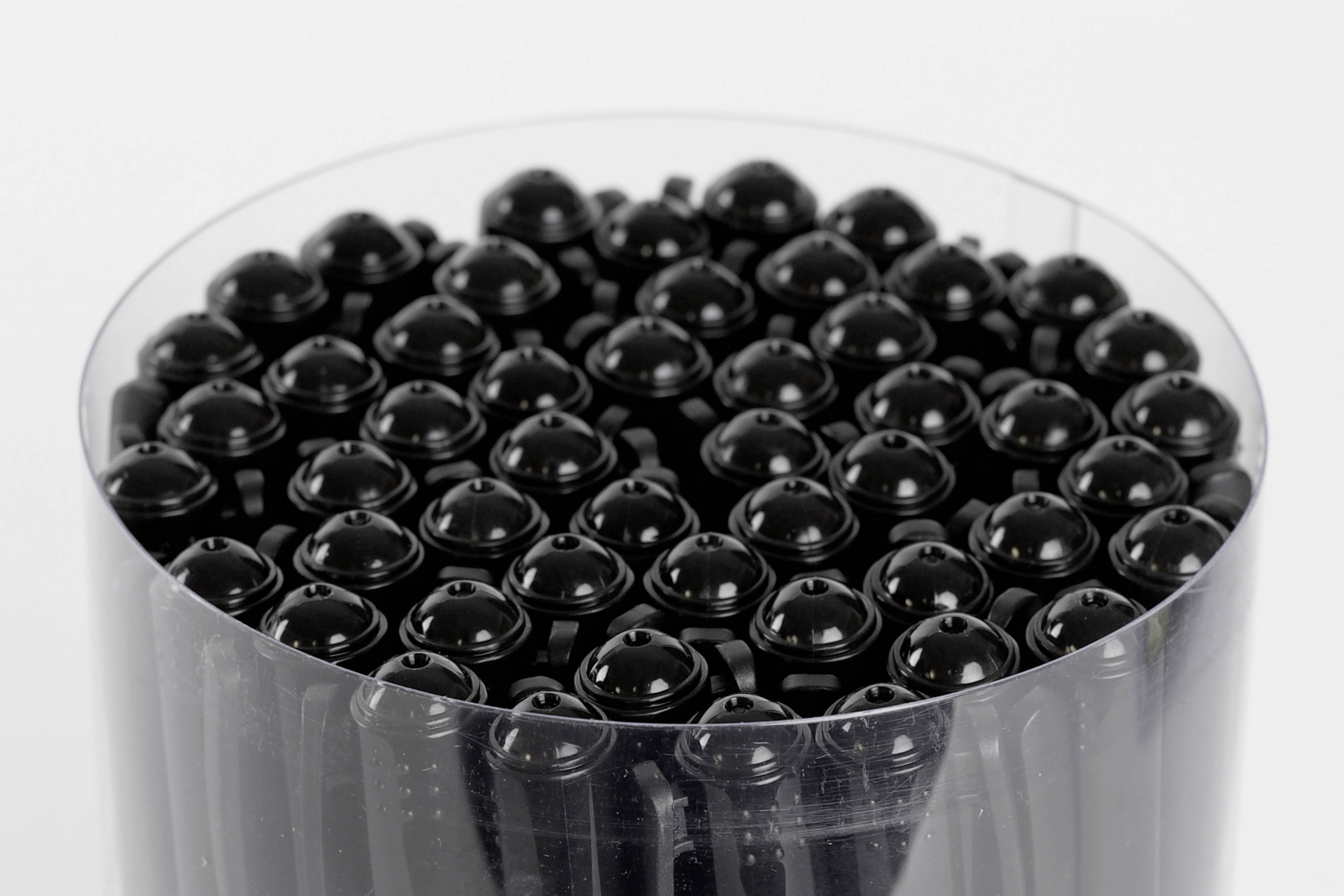 Un récipient rond rempli de stylos noirs, tous disposés de manière uniforme et ordonnée, vu de dessus sur un fond blanc.