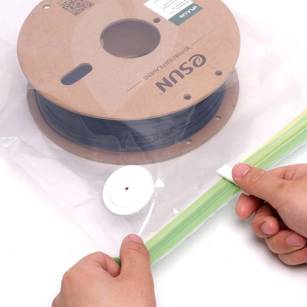 Un rouleau de filament d'imprimante 3D dans un sac sous vide avec une valve de dégazage. Une main tient le sceau du sac.