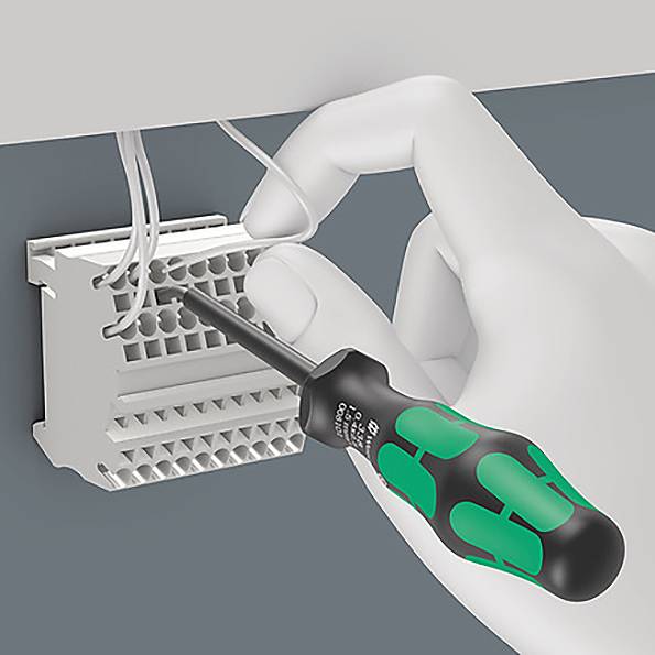 Une main utilise un tournevis pour serrer des fils dans un bornier, illustrant un processus de connexion électrique.
