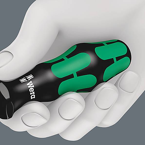 Une main tenant un tournevis ergonomique vert et noir de la marque Wera sur la poignée.
