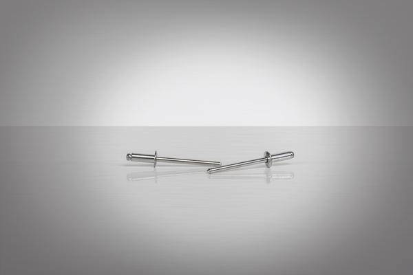 Deux rivets métalliques reposent sur une surface grise réfléchissante avec un fond dégradé.