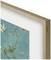 Un tableau encadré dans un élégant cadre en bois représente un fragment de branches fleuries sur un fond turquoise, dans l'esprit de Van Gogh.