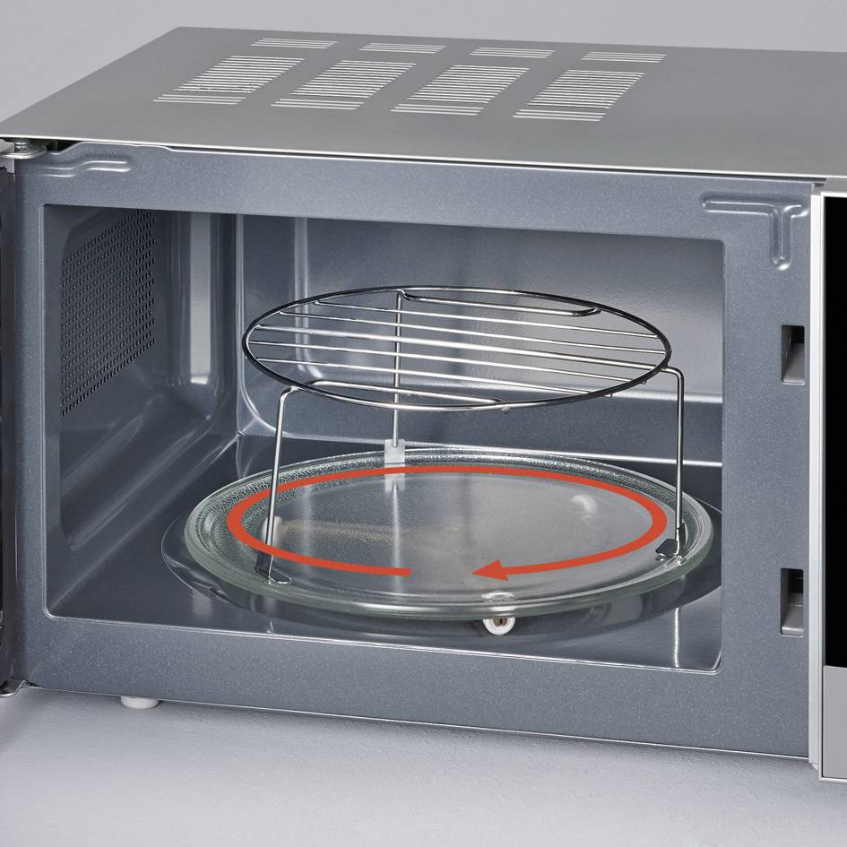 Four micro-ondes ouvert avec plateau tournant et grille de grill à l'intérieur, prêt à être utilisé. Paroi arrière en métal avec des fentes d'aération.