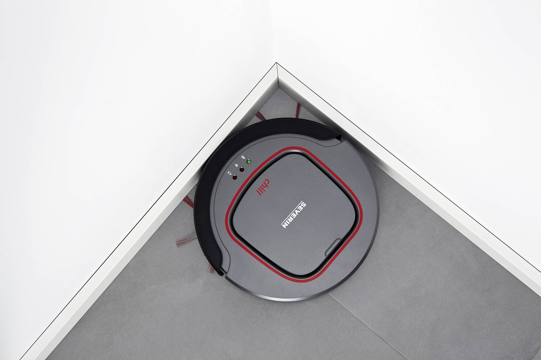 Un robot aspirateur rond nettoie un coin d'une pièce sur un sol gris.