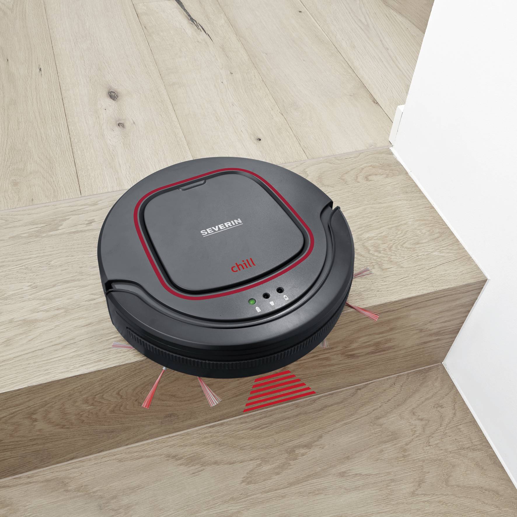 Un robot aspirateur noir sur un sol en bois, près d'un escalier.