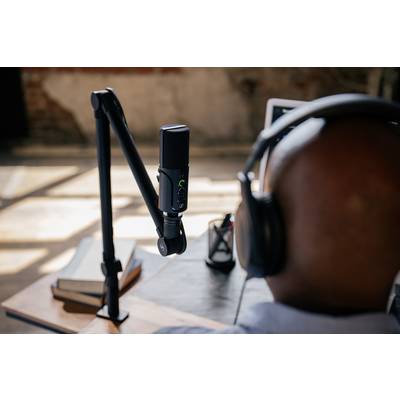 Un homme portant des écouteurs est assis à une table avec un microphone, concentré sur ce qu'il enregistre ou sur ce qu'il dit.