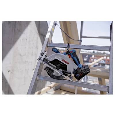 Une scie circulaire Bosch est montée sur un échafaudage métallique sur un chantier de construction. Des poutres en bois et un bâtiment sont visibles en arrière-plan.