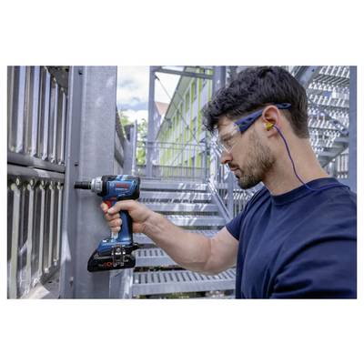Un homme portant un équipement de sécurité utilise une perceuse électrique sur une structure métallique en extérieur. Il porte des lunettes et une protection auditive pour sa sécurité.