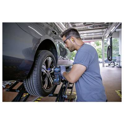 Un mécanicien utilise un outil électrique pour travailler sur la roue d'une voiture dans un atelier de réparation automobile. Il porte des protections auditives et des gants, concentré sur sa tâche.