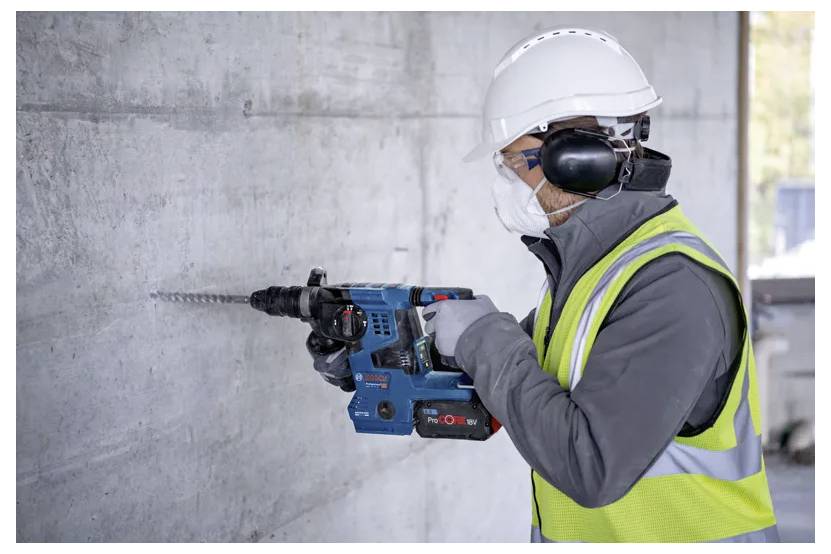 Un ouvrier du bâtiment équipé de vêtements de sécurité utilise une perceuse électrique sur un mur en béton.