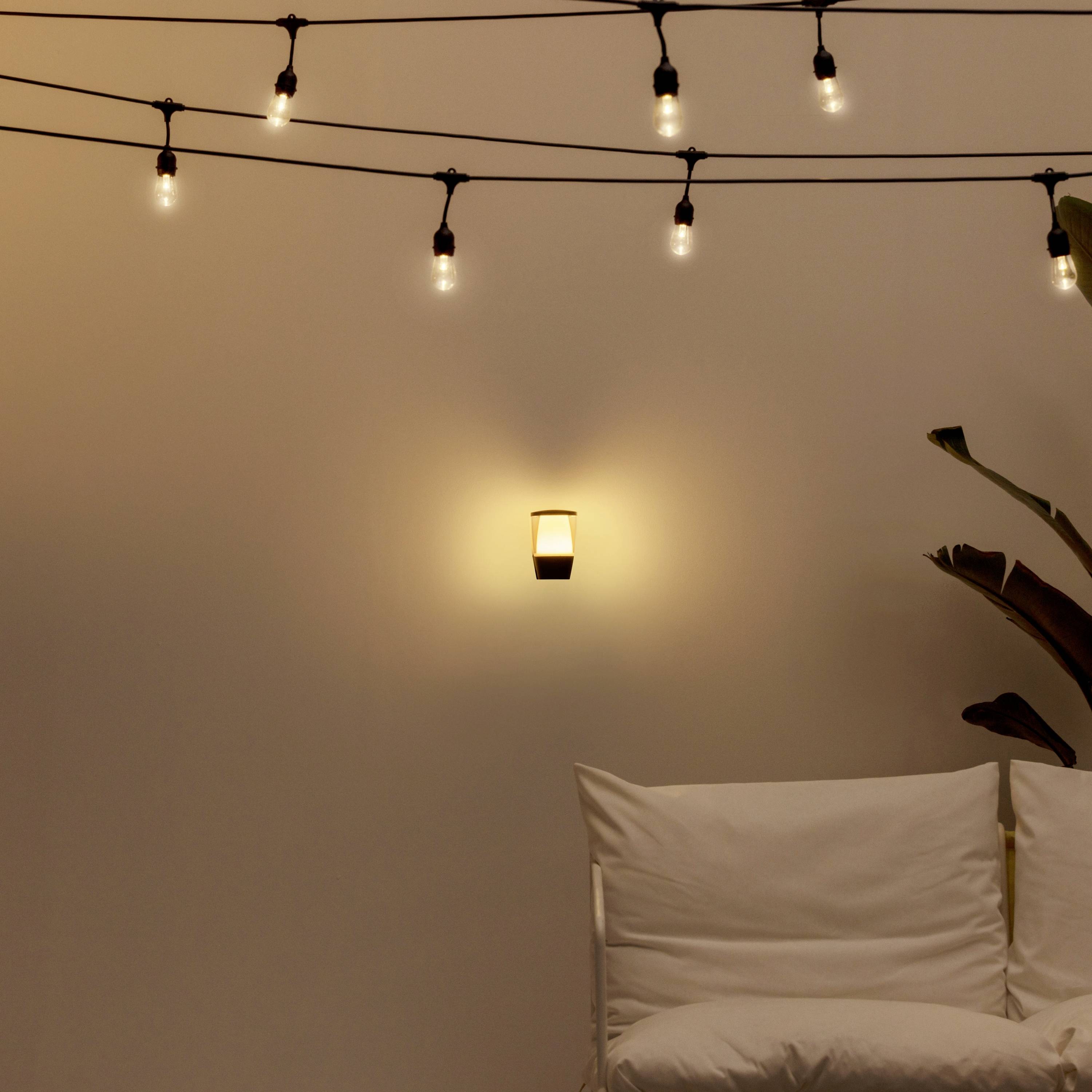 Guirlande lumineuse au mur, applique murale illuminée, avec un coussin blanc posé sur une chaise en dessous. Ambiance détendue et chaleureuse.