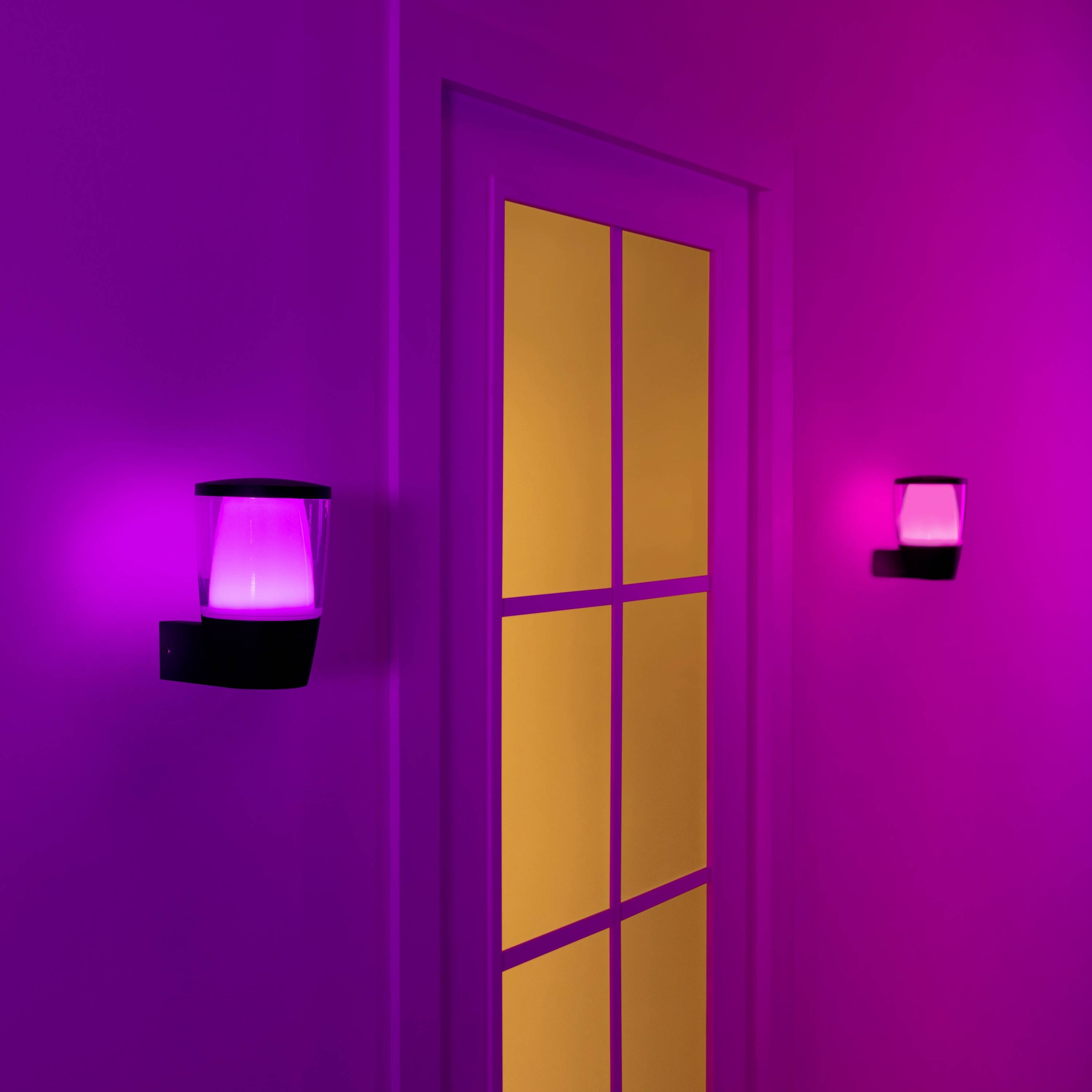 Une porte fermée avec des fenêtres en verre, éclairée par deux appliques murales roses. La porte brille d'une lueur orange, la pièce paraît moderne et futuriste.