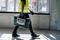 Une personne portant un gilet de sécurité transporte une mallette à outils à travers un bâtiment en construction. De grandes fenêtres sont visibles en arrière-plan.