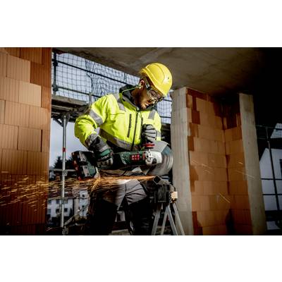 Un ouvrier portant un équipement de protection coupe du béton avec une meuleuse d'angle, des étincelles jaillissent. Un chantier de construction est visible en arrière-plan.