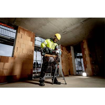 Un ouvrier porte des équipements de protection et utilise un outil de coupe pour scier une barre métallique dans un bâtiment en construction. Des étincelles jaillissent.
