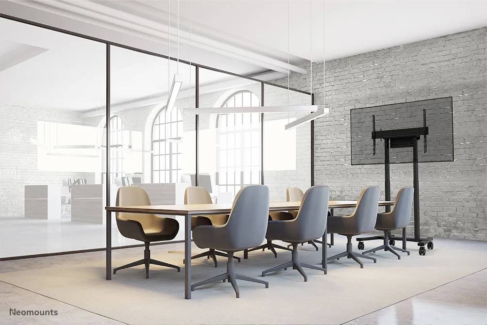 Une salle de conférence moderne avec une grande table, huit chaises, un écran plat fixé au mur et de grandes fenêtres en arrière-plan.