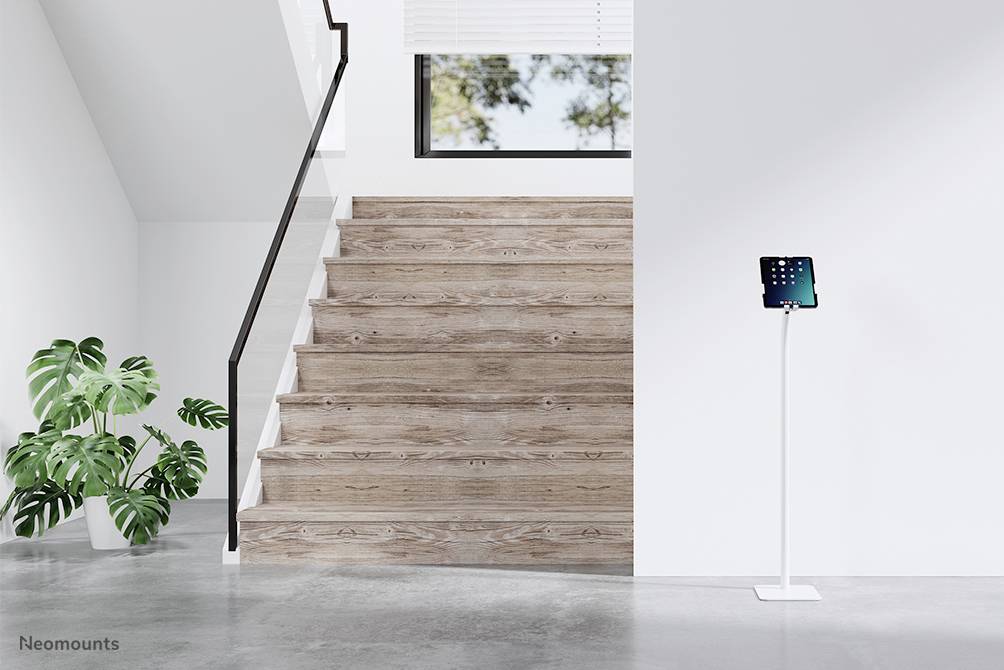 Escalier en bois avec garde-corps noir, à côté duquel se trouve une plante verte. À droite, une tablette est posée sur un support blanc.