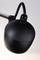 Une lampe noire, sphérique, avec un câble, est suspendue à une tige métallique.