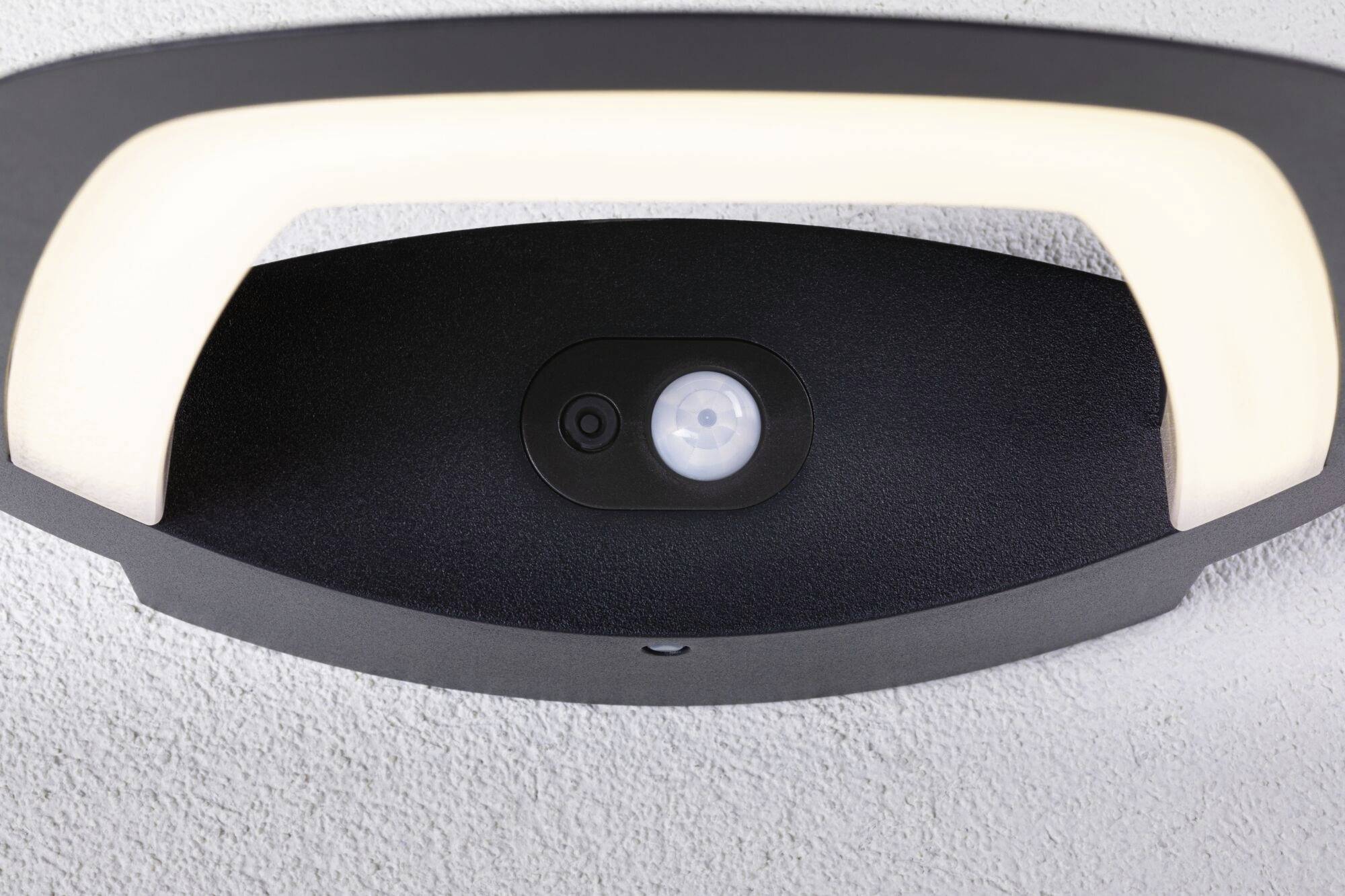 Plafonnier avec capteur intégré pour détecteur de mouvements, installé sur un plafond blanc, design moderne à forme ovale avec contour noir.