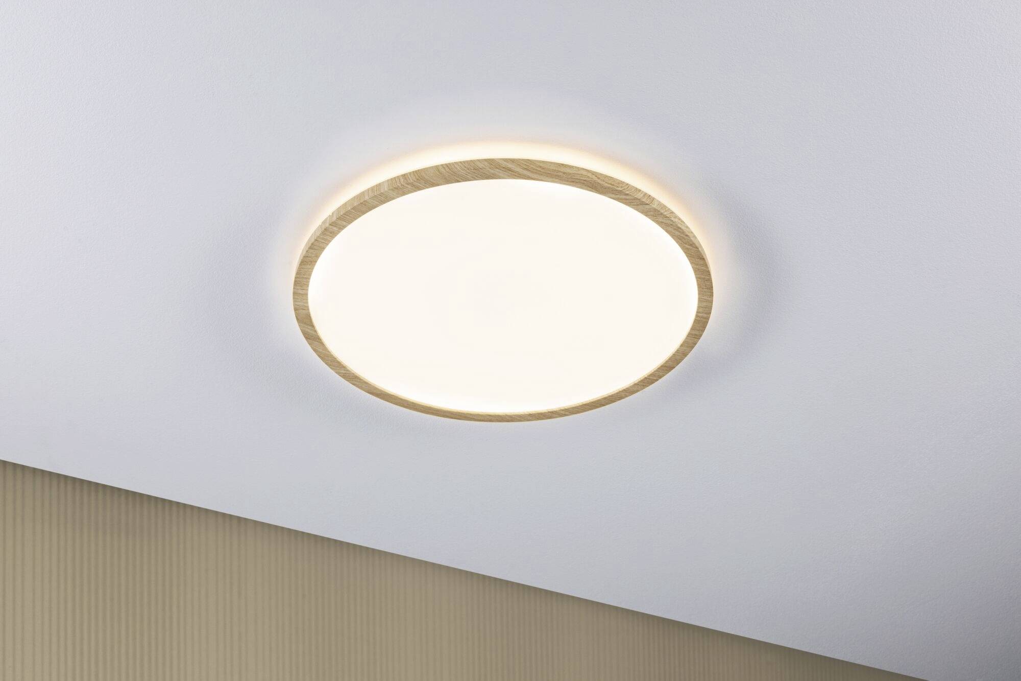 Plafonnier rond avec un cadre en bois et une lumière chaleureuse, monté sur un plafond blanc. Style épuré et minimaliste.