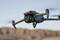 Un drone plane dans les airs devant un paysage montagneux. Le drone possède quatre rotors et une caméra à l'avant.