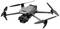 Drone grise à quatre rotors avec caméra, en vol stationnaire. Elle présente un design compact avec des marquages d'accent orange sur les pales des rotors.