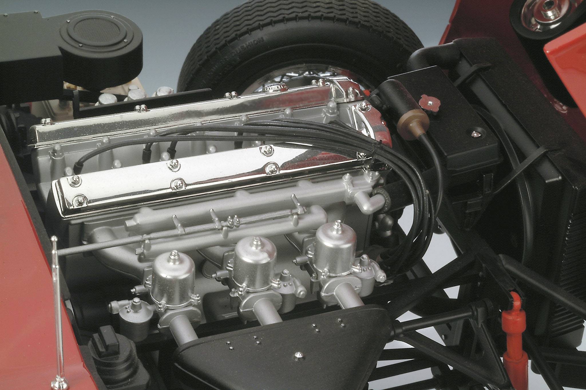 Un moteur rutilant avec des câbles d'allumage apparents et trois carburateurs dans un compartiment moteur ouvert d'un véhicule rouge.