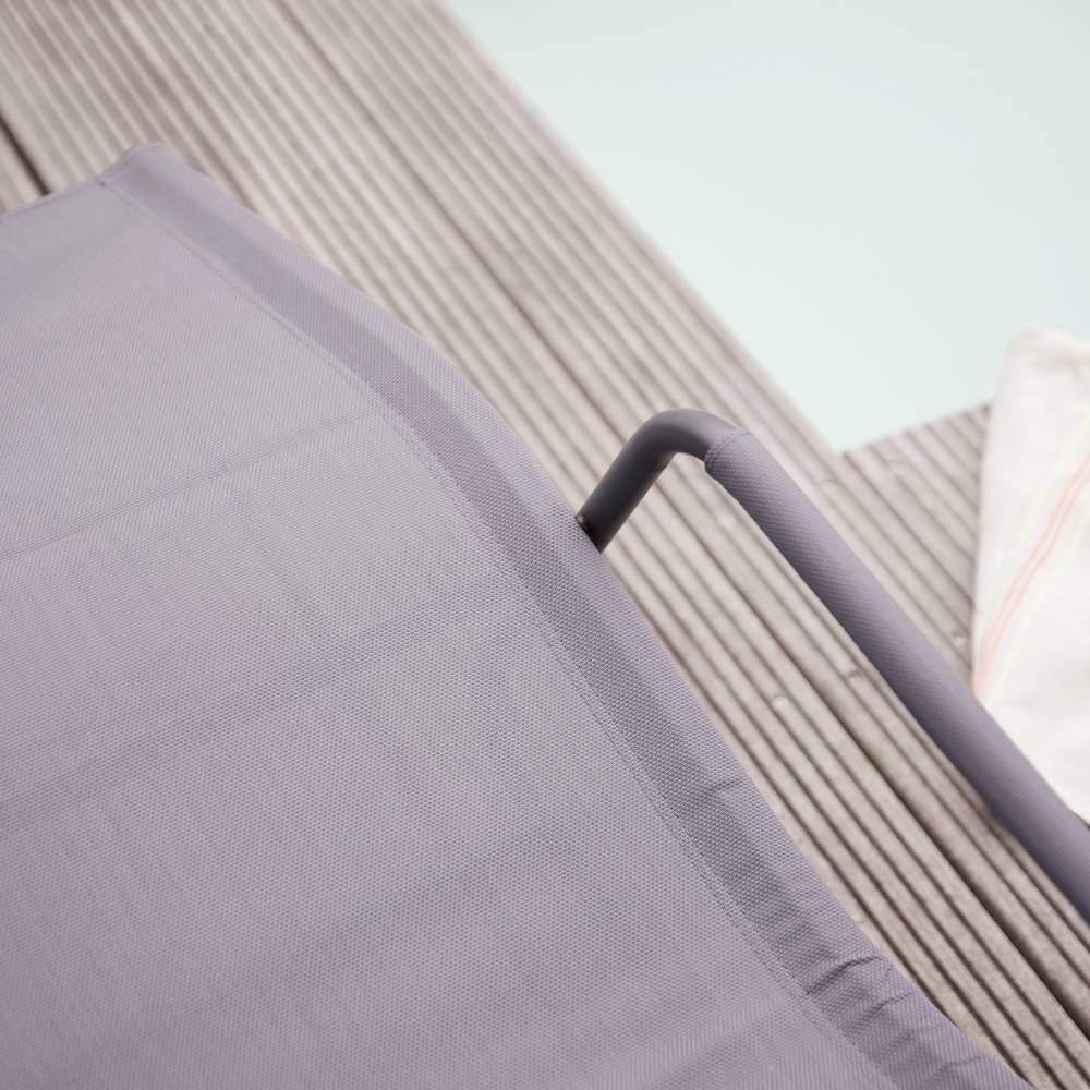 Un coussin de chaise longue gris est posé sur des lames de terrasse à côté d'une piscine. Une serviette est partiellement visible. Atmosphère décontractée.