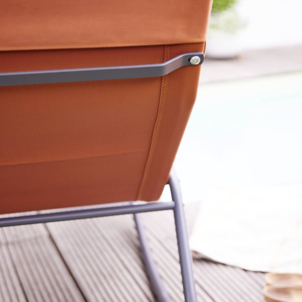 Partie d'un transat orange sur une terrasse en bois, à côté d'une zone de piscine floue en arrière-plan.