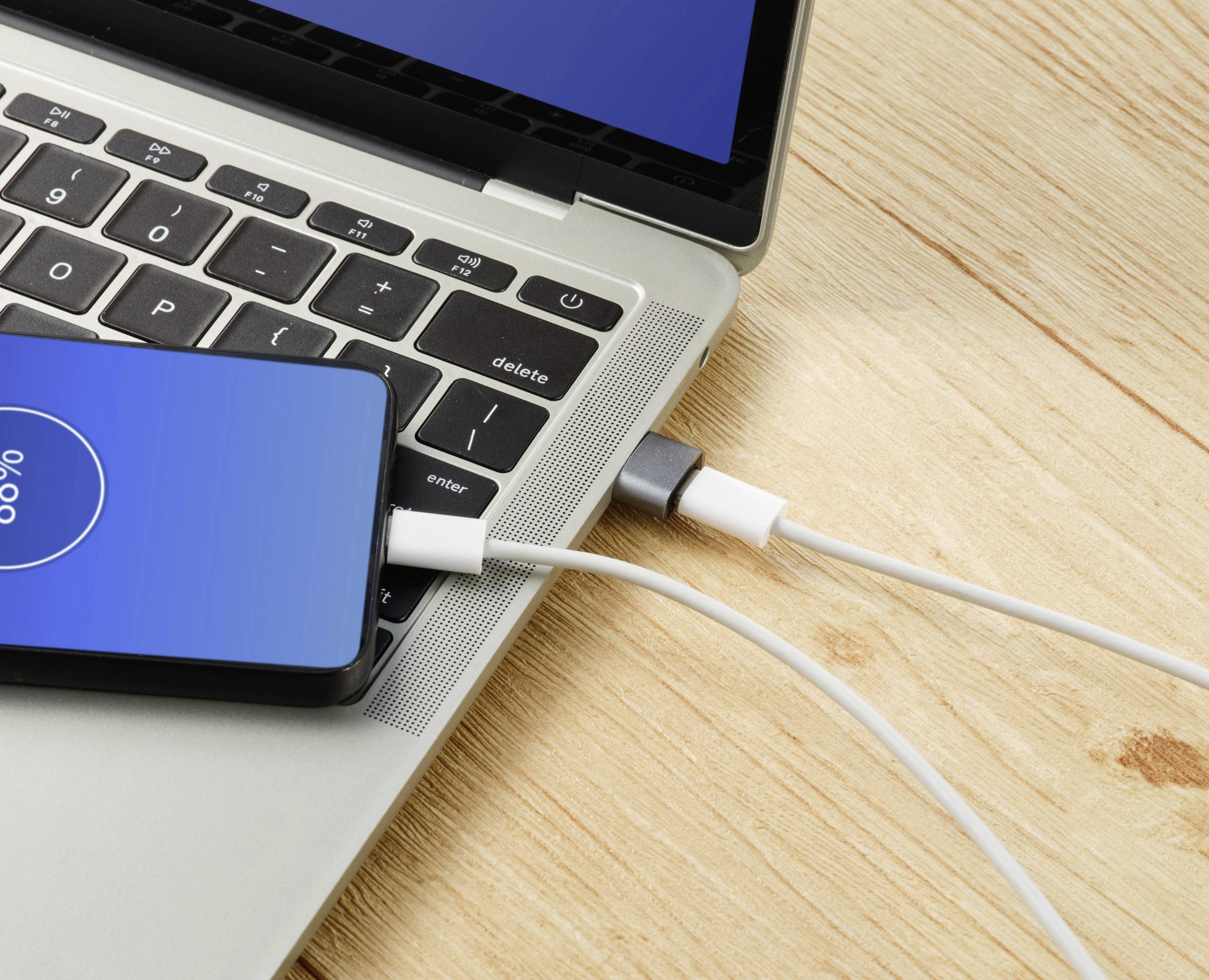 Un smartphone est connecté à un ordinateur portable via un câble USB. L'écran affiche la progression de la charge.