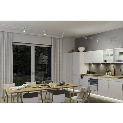 Cuisine moderne avec table à manger, chaises et éclairage lumineux. Sur la table, de la vaisselle et un ordinateur portable sont posés. De grandes fenêtres donnent sur le jardin.