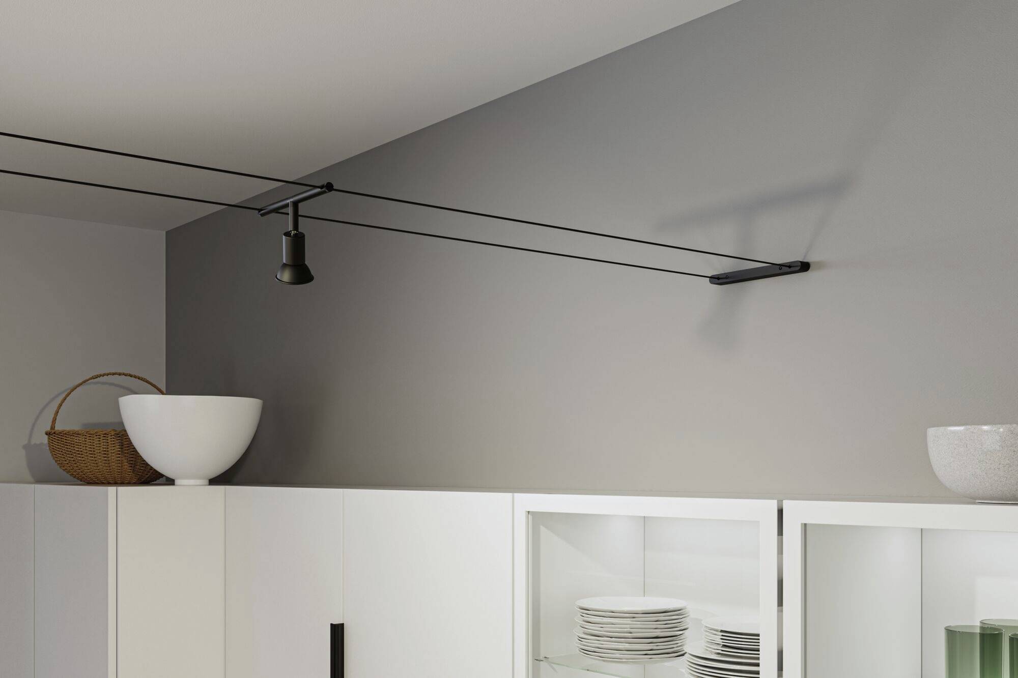 Éclairage plafonnier dans une cuisine moderne avec des rails électriques noirs et un projecteur orientable. Armoires avec façades vitrées et bols posés sur le dessus.