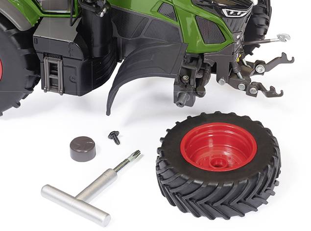 Tracteur jouet avec roue détachée, vis, tournevis et outils au premier plan.